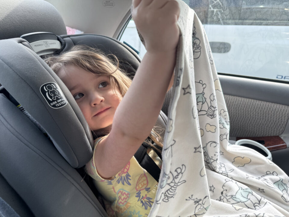 Olivia in her carseat holding up her blanket