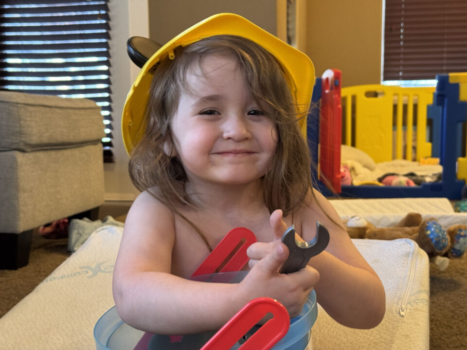 Olivia wearing a helmet and holding toy tools